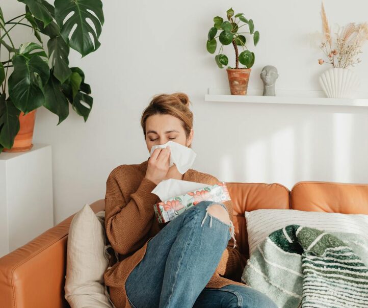 Woman sitting on a sofa blowing her nose because of seasonal allergies
